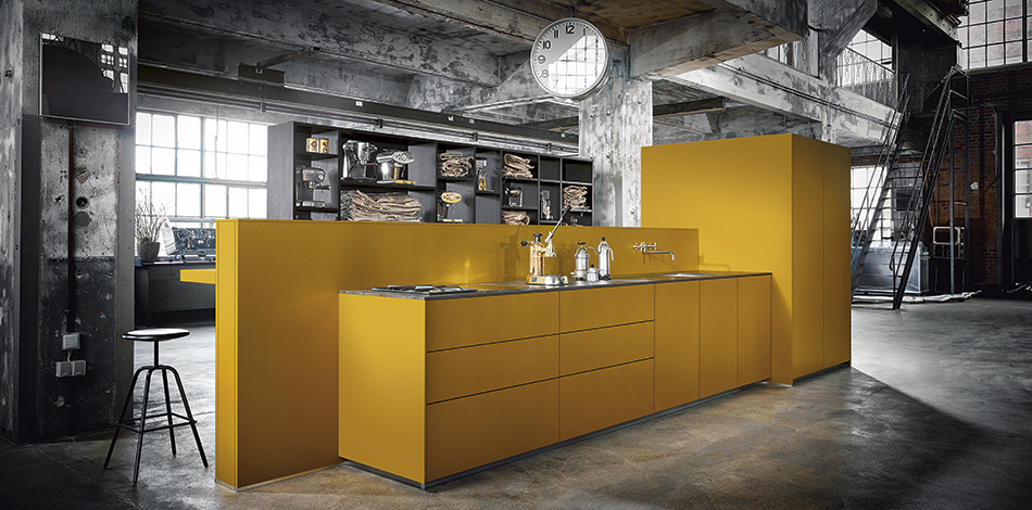 The kitchen block in saffron yellow satin with the elegant horizontal bar allows guests to share in the cooking processing, turning the act of cooking into a sensuous experience. The entire process is supported by an open shelf unit that divides the room while allowing insights that present the room with charm and grace. The technology is hidden away inside a tall unit, and the extractor hood is also hidden from sight.